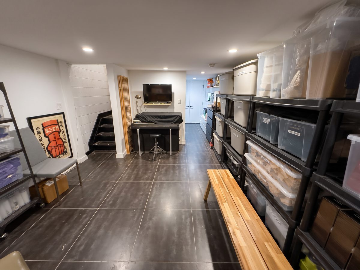 Basement after organizing, with a clear walkway, styled corner and labeled storage along one wall